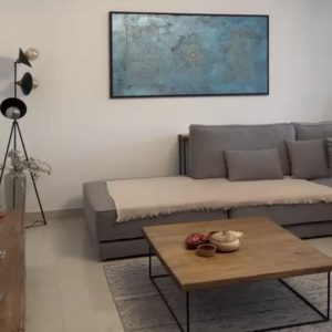 اتاق نشیمن با مبل خاکستری و تابلو هنری آبی در دیوار.